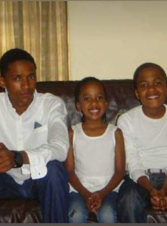 A photograph of three children in white on a leather couch